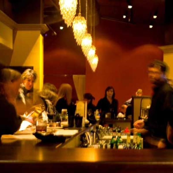 Warmly lit bar area at East India Co. Grill & Bar with patrons and a bartender.