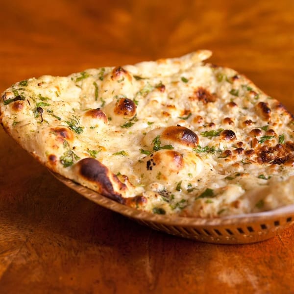 Close-up of garlic naan bread with cilantro, served in a metal basket on a wooden table.