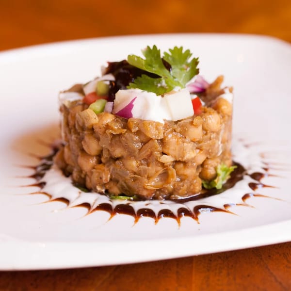 Indian chickpea dish, topped with cilantro, red onion, and white cheese, on a white plate.