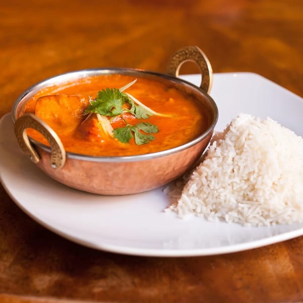 Indian butter chicken or paneer curry in a copper bowl with a side of white rice.