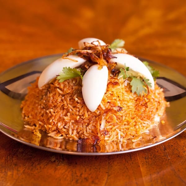 Indian biryani with rice, fried onions, cilantro, and sliced hard-boiled eggs on a silver plate.