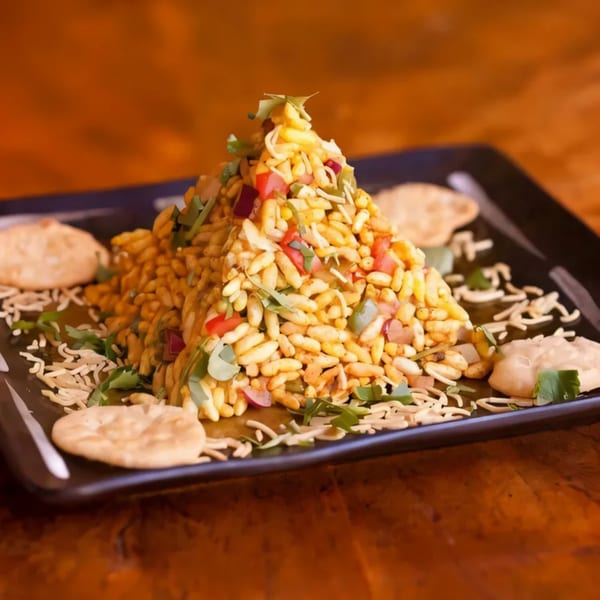 A pyramid of Bhel Puri, a popular Indian street food, on a black plate with crackers.