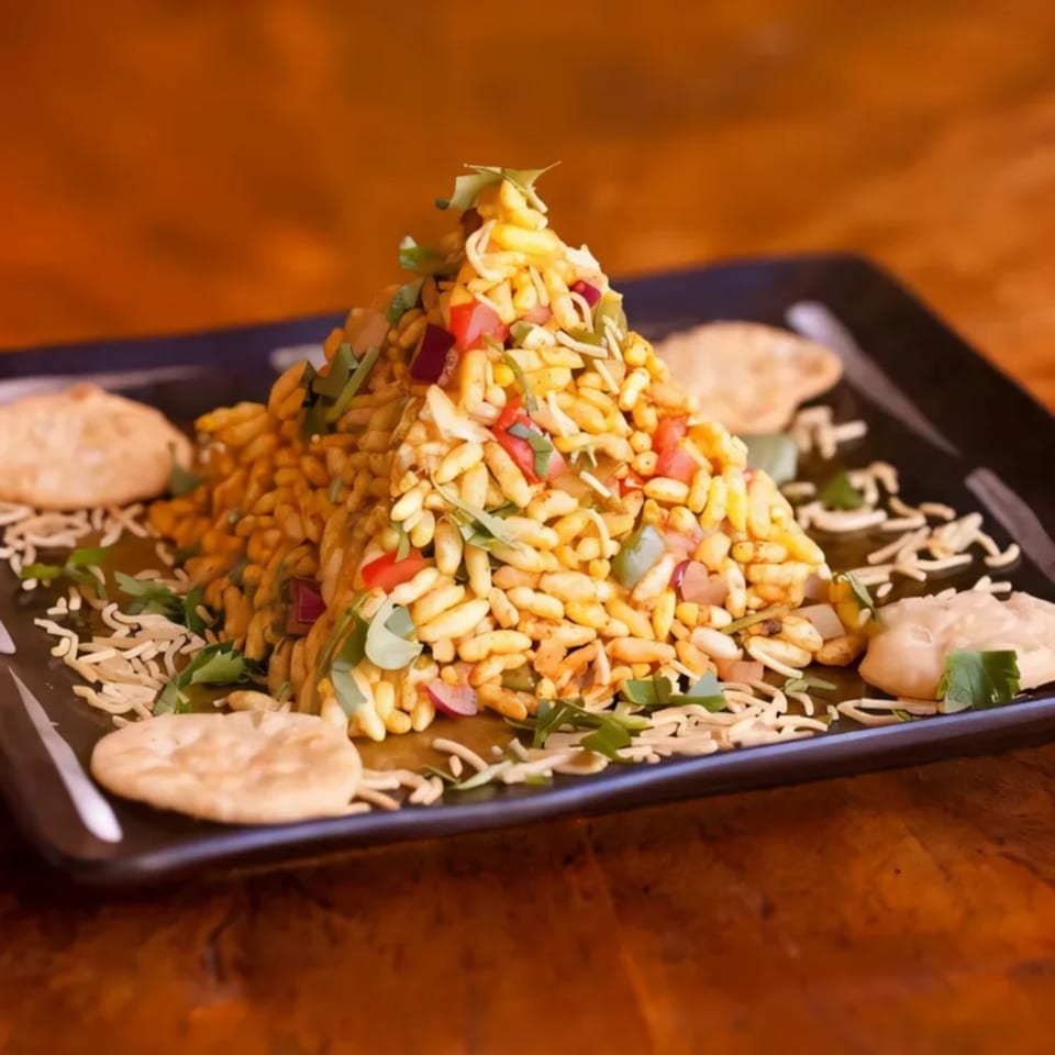A pyramid of Bhel Puri, a popular Indian street food, on a black plate with crackers.