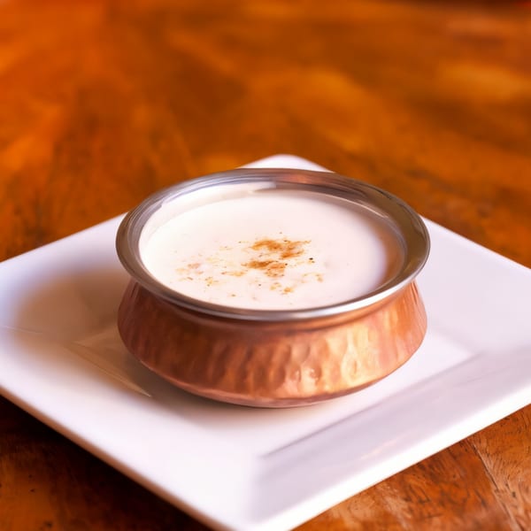Indian lassi drink in a copper cup with spices on top, served on a white plate.