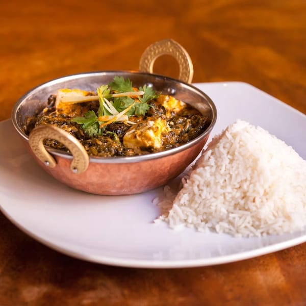Indian palak paneer in a copper bowl with a side of white rice on a white plate.
